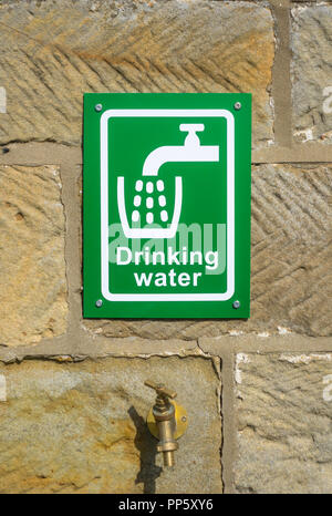 A green and white outdoor drinking water sign on a sandstone wall above a brass tap Stock Photo