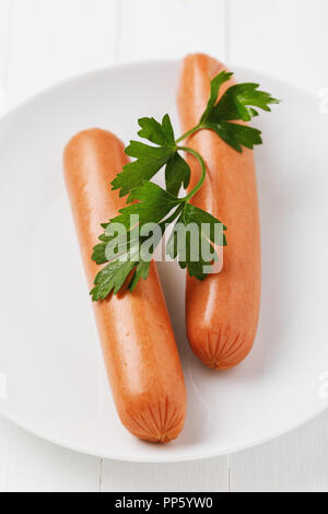 Breakfast of two boiled sausages with parsley in a white plate on a wooden table Stock Photo