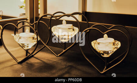 Three flaming candles on hearts metal candle stand. Holidays decoration. Stock Photo
