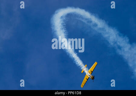 Yakovlev Yak-52 aerobatic plane arcing over with smoke trail in blue sky. Flying aerobatics. Loop the loop. Looping Stock Photo