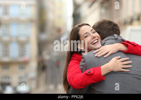 Cheerful couple meeting and hugging in the street with copy space at side Stock Photo