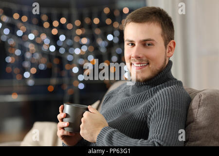 Man posing looking at you in winter sitting on a couch in the living room at home Stock Photo