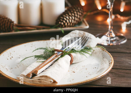 Thanksgiving table setting among white candles and cones. Ceramic plate with fork and knife on a linen napkin. The concept of a festive dinner. Stock Photo