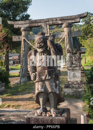 Nio temple guardian stone statue with torii gate behind, Kunisaki Hanto, Oita,  Kyushu, Japan Stock Photo