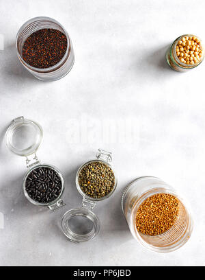 Frame of cereals selection and beans in jars: black quinoa, chickpea, green lentils, buckwheat, black beans top view on grey concrete background Stock Photo