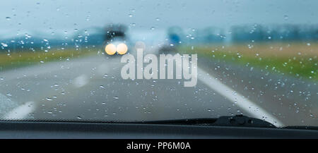 Blurred traffic lights seen through the rain drops on the windscreen of a car on a highway Stock Photo