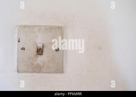 Close up of very dirty square lightswitch on stained white wall. Stock Photo