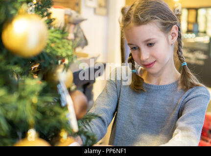Little girl hanging decorative ball on the christmas fur-tree. Stock Photo