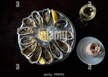 Plate of oysters from the Arcachon bay. Oysters on a bed of ice with lemon, butter, a glass of wine and some pate Stock Photo