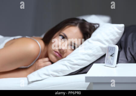 Insomniac woman bored looking at alarm clock in the bed in the night Stock Photo