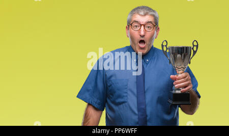 Handsome senior successful man holding trophy over isolated background scared in shock with a surprise face, afraid and excited with fear expression Stock Photo