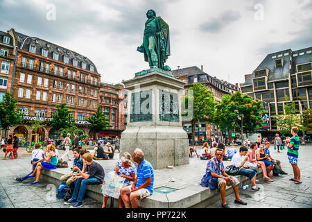 People sit around the statue of Gutenberg in Place Gutenberg, Strasbourg, France surrounded by beautiful and historic French buildings. Stock Photo