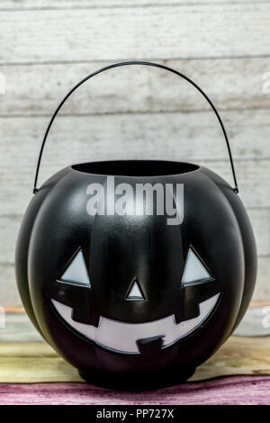 Orange plastic pumpkin trick or treat bucket with a jack o lantern face. Isolated on brick background. Halloween concept Stock Photo