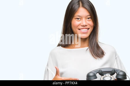Young asian woman holding vintagera telephone over isolated background very happy pointing with hand and finger Stock Photo