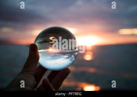 Sunset over Ocean with Reflection Captured in Glass Ball on Sand Stock ...