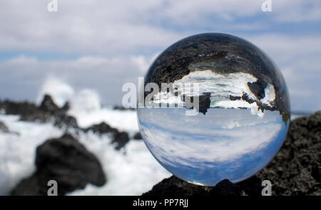Lava Coastline with Breaking Waves Captured in Reflection in Glass Ball Stock Photo