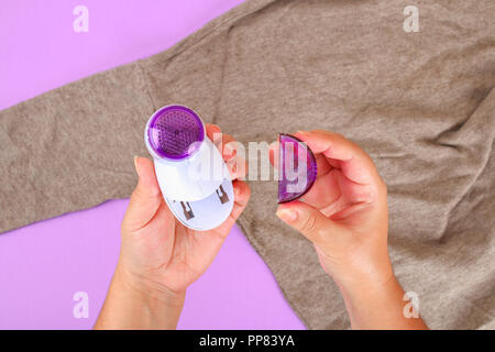A machine for removing lint in the hand. Sweater with bobble on a purple pastel background Stock Photo