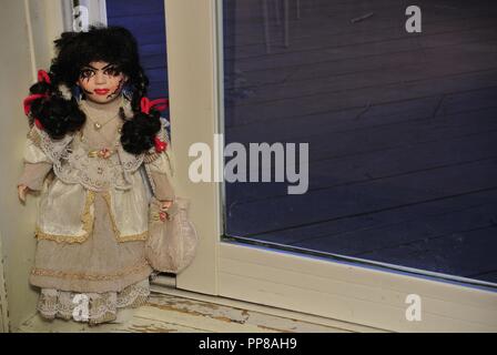 A creepy antique porcelain doll with long black hair and a scary, beautiful face with scars,,dressed in a white vintage dress, coming at you Halloween Stock Photo