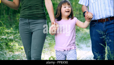 Beautiful little girl with down syndrome walking with parents Stock Photo