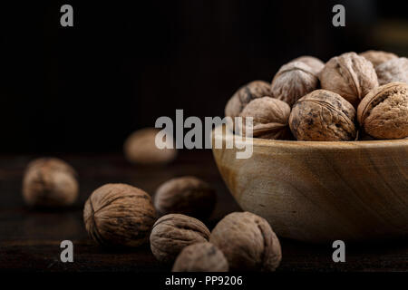 whole walnuts in a plate on an old country table and against a dark background. place for text Stock Photo