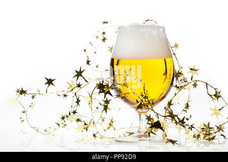 Full snifter glass of pale lager of pilsner beer with a large head of foam and golden christmas tinsel on white background Stock Photo