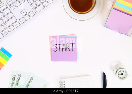 Text Start on the sticker note on the white desktop next to the coffee mug and the keyboard. Top view, flat layout Stock Photo