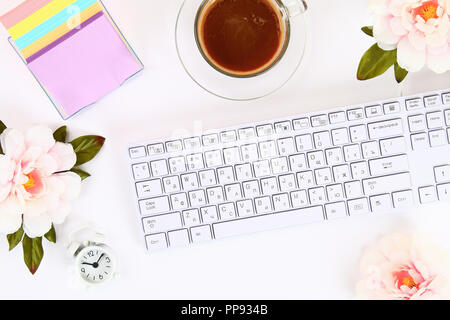 Pink flowers, clock on a white desktop next to a mug of coffee and a keyboard. Top view, flat layout. Copy the space Stock Photo