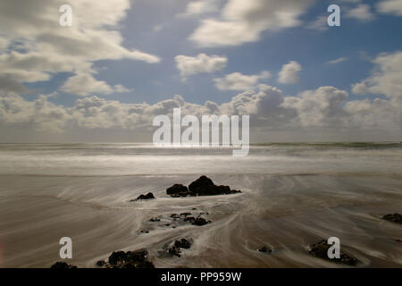 Receding waves leave a swirling pattern around a rock with dramatic sky and sea Stock Photo