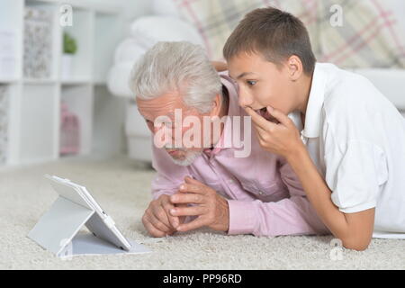Grandfather with grandson using tablet while lying on floor  Stock Photo