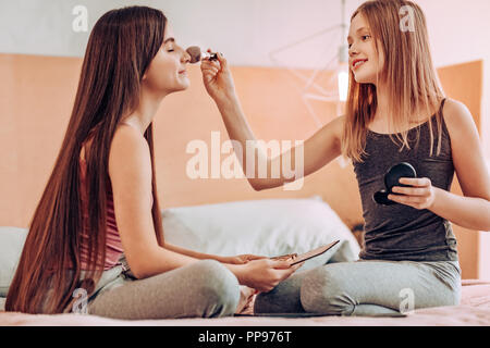 Concentrated little female doing makeup for her friend Stock Photo