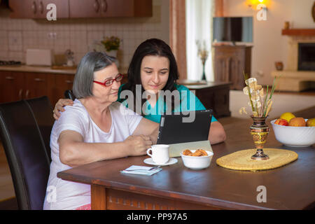 Female nurse and senior woman using tablet PC in kitchen at nursing home. Stock Photo
