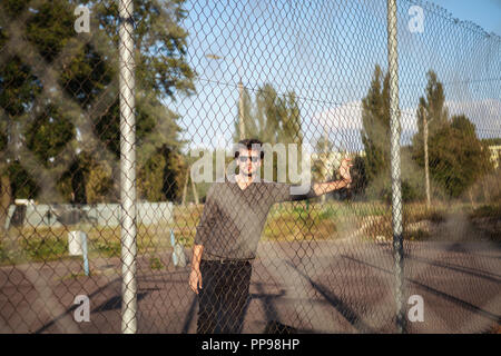 Handsome man in sunglasses leaning on iron fence and posing on camera Stock Photo
