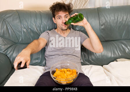 Excited young man with the remote and beer and chips on the couch Stock Photo