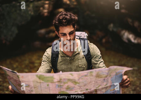 Handsome young man with backpack looking at the map for directions while hiking in mountain. Male hiker using a map to locate the destination. Stock Photo