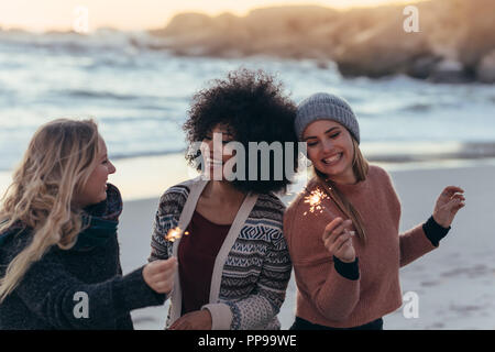 Happy friends partying on the beach with sparklers. Diverse group of woman friends together at the beach celebrating new year's day at the beach. Stock Photo