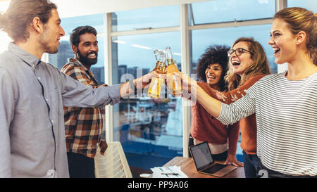 Business colleagues toasting beer to celebrate success in office. Businessmen and women taking a break from work to celebrate success Stock Photo