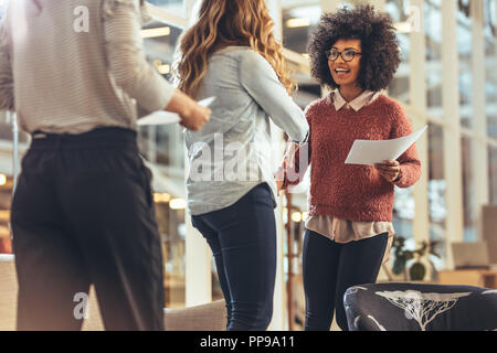 Woman entrepreneur holding official papers greeting a business client at work place. Businesswoman shaking hands with a woman standing in office. Stock Photo