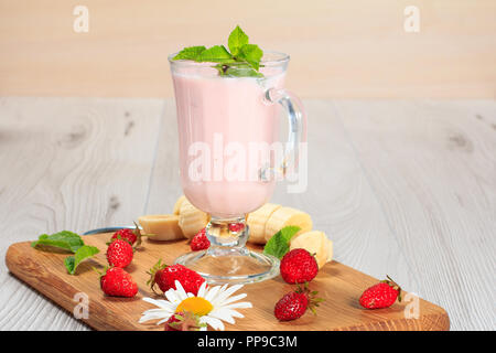 Glass of delicious milk shake with mint and fresh strawberries,  banana, chamomile on a wood cutting board Stock Photo