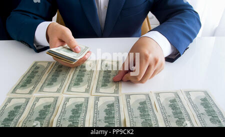 Closeup photo of wealthy businessman laying US dollars banknotes on office desk in long rows Stock Photo