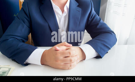 Closeup image of wealthy successful businessman in blue suit sitting with folded hands at modern office Stock Photo