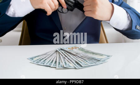 Closeup image of businessman with big stack of money putting handgun in his jacket pocket Stock Photo