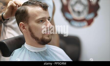 Men's haircut in barbershop. Master barber does a haircut to the client. Work with scissors and clipper. Close-up of the workflow Stock Photo