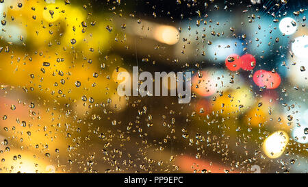 autumn rainy weather - view of blurred urban lights through the home window with raindrops (focus on the rain drops on the glass) Stock Photo