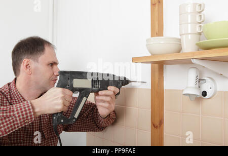 Man with power drill drilling the hole in a kitchen wall Stock Photo