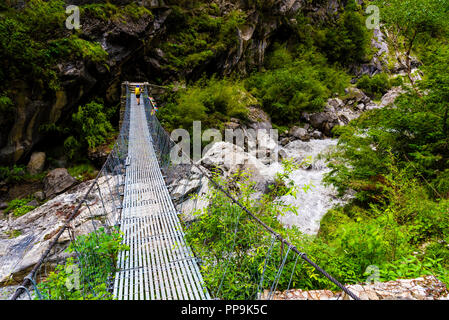 Annapurna Conservation Area, Nepal - July 19, 2018 : Woman backpacker on trekking path crossing a suspended bridge in Annapurna Conservation Area, a h Stock Photo