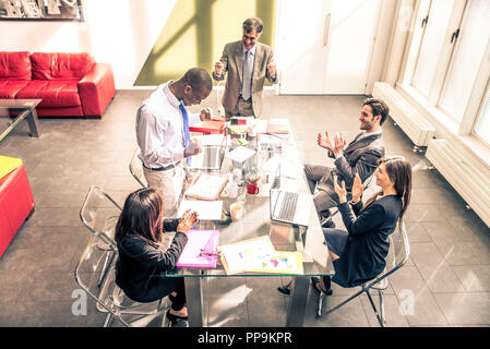 Business team having a meeting in a office, afro-american man exulting and his colleagues clapping hands - Successful businessman getting a promotion  Stock Photo