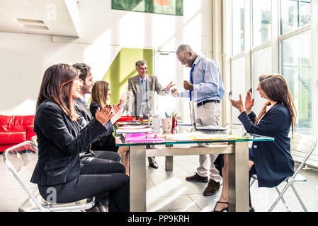 Business team having a meeting in a office, afro-american man exulting and his colleagues clapping hands - Successful businessman getting a promotion  Stock Photo
