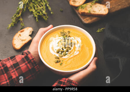 Person holding bowl of warm pumpkin soup in hands. Comfort food, autumn food concept Stock Photo