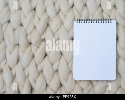 Notebook on merino wool handmade knitted large blanket, super chunky yarn, trendy concept. Close-up of knitted blanket, merino wool background Stock Photo