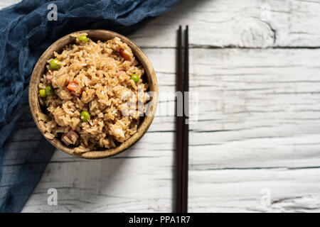 high angle view of a boxwood bowl with a Chinese fried rice and a pair of chopsticks on a rustic white wooden table Stock Photo